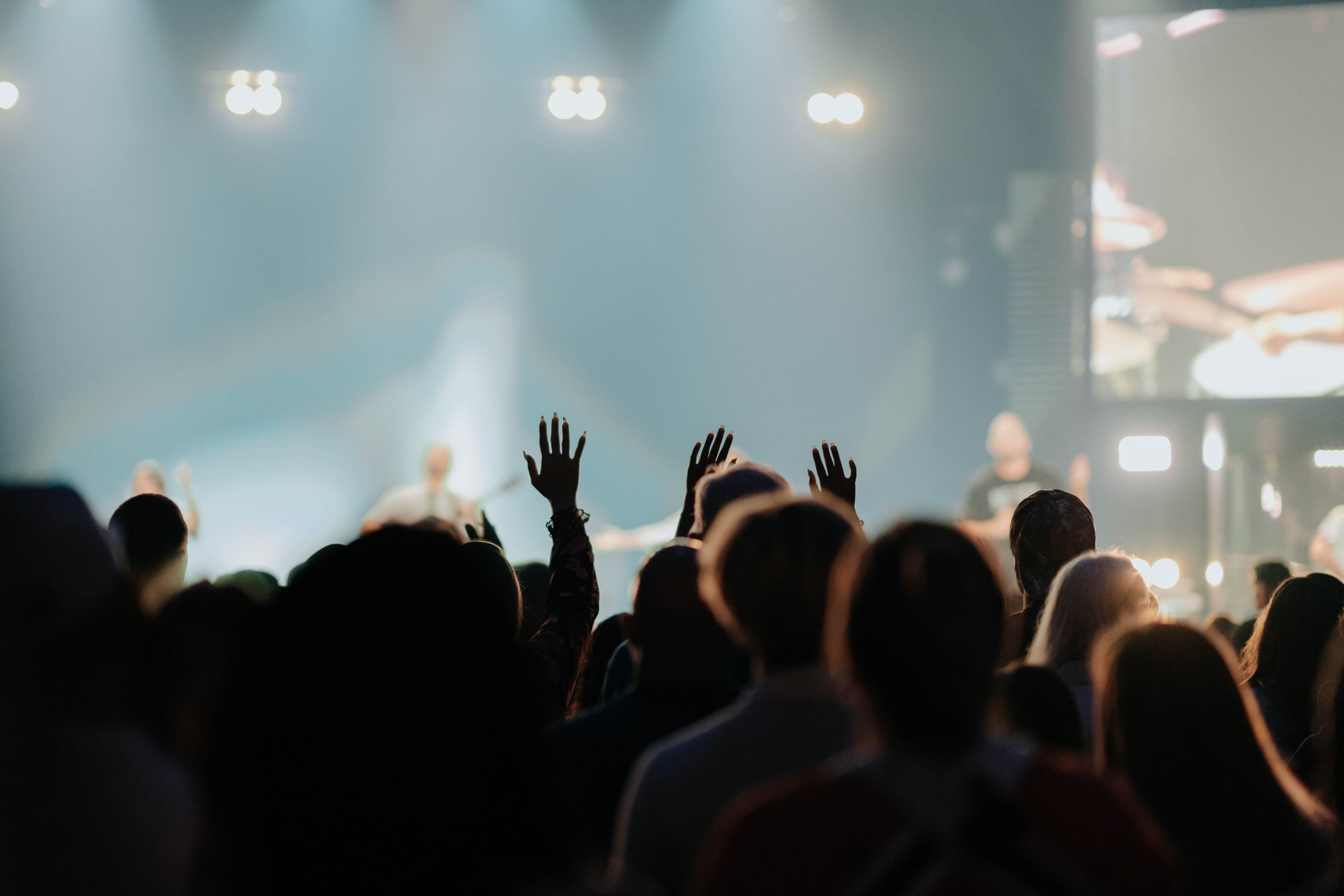 Hands raised in worship as a band plays on a hazy, softly lit stage